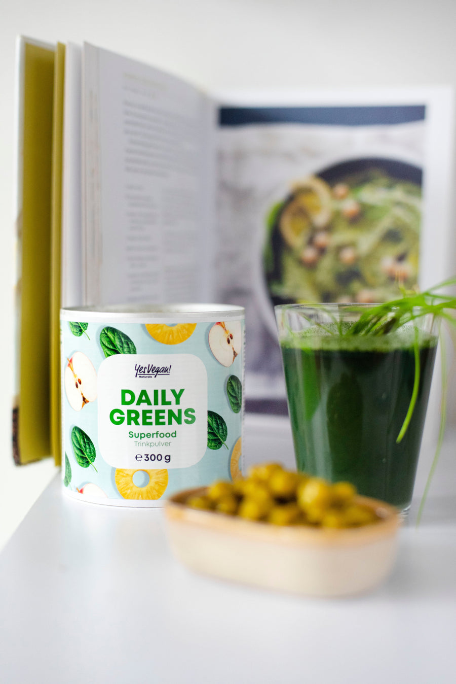 Yes Vegan Daily Greens Superfood Trinkpulver neben grünem Drink und Kochbuch