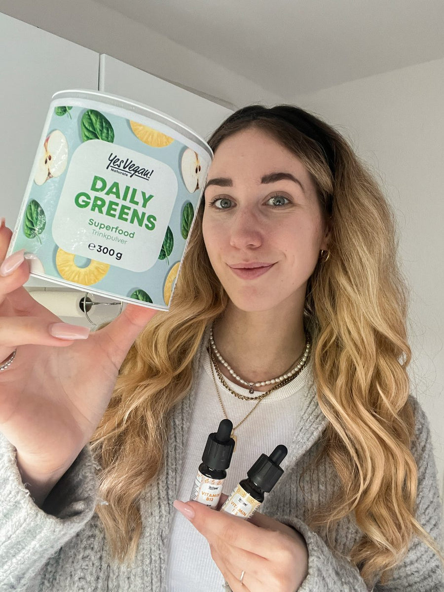 Frau hält Yes Vegan Daily Greens Dose und Vitamintropfen