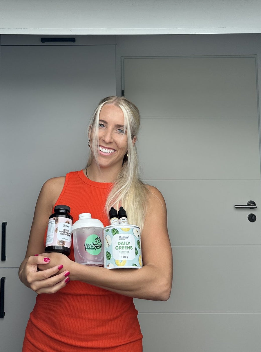Frau hält Yes Vegan Daily Greens, Super Mushroom Complex, Vitamintropfen und Shaker