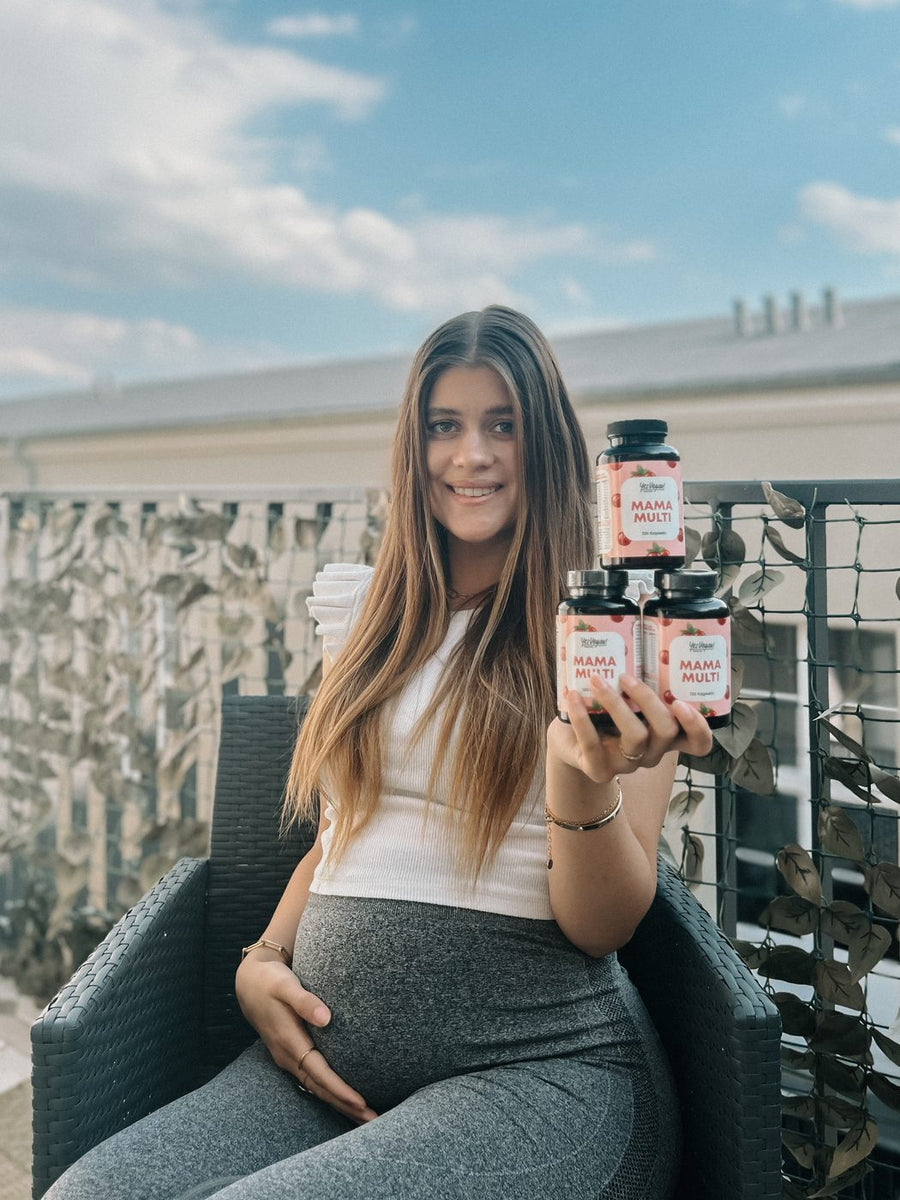 Schwangere Frau hält drei Dosen Yes Vegan Mama Multi auf dem Balkon